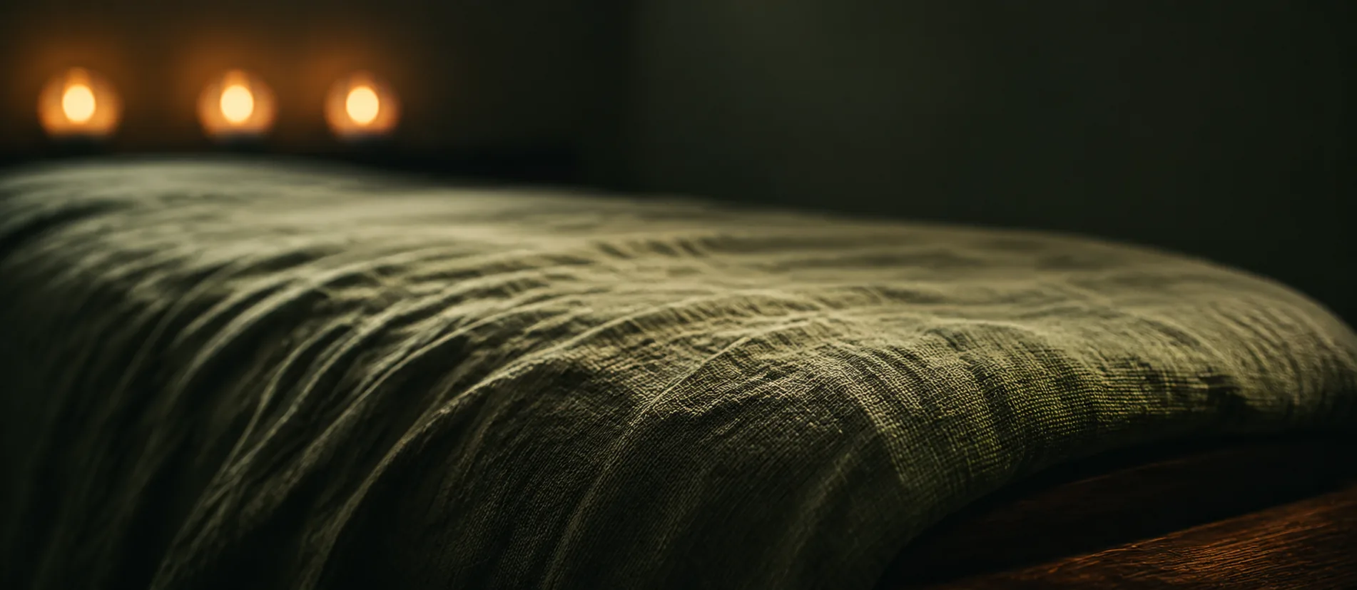 Närbild på grönt linnetyg över massagebänken med levande ljus i bakgrunden